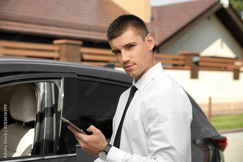 Attractive young man with smartphone near luxury car outdoors