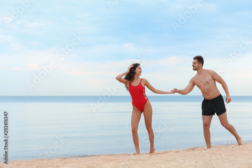 Happy young couple walking together on beach near sea © New Africa