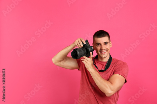 Young photographer with professional camera on pink background