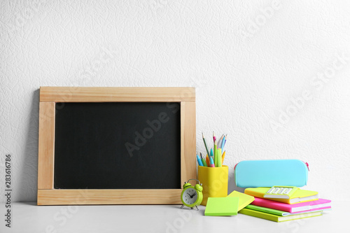 Blank small chalkboard and different school stationery on wooden table near white wall. Space for text