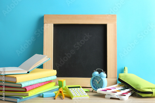 Different school stationery and small blank chalkboard on table near light blue wall. Space for text