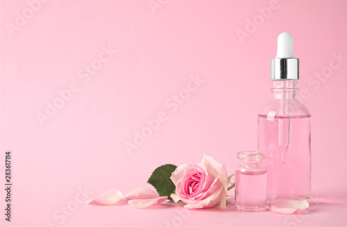 Bottles of essential oil and rose on pink background. Space for text