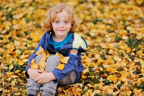 baby - little boy with curly blond hair smiling against the background of yellow autumn leaves in the Park