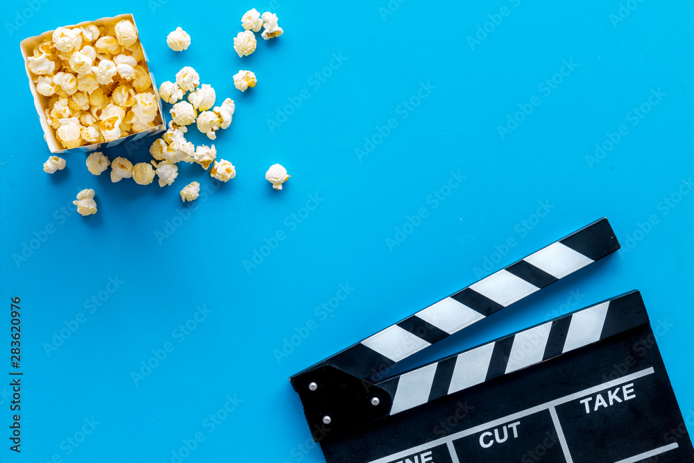 Filmmaker profession with clapperboard and popcorn on blue background top view copyspace