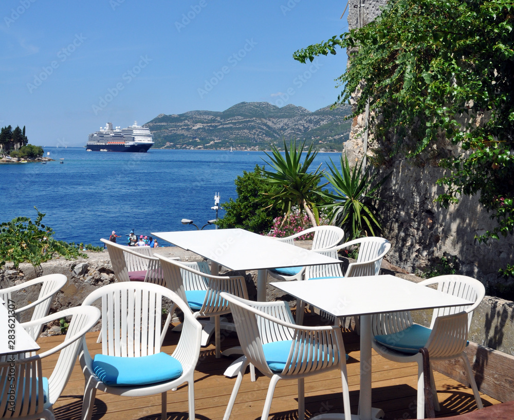 close-up of white tables and chairs on the terrace overlooking the blue Adriatic sea on which the cruise ship sails.
