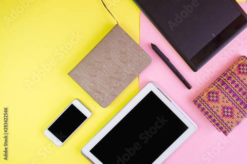 Flat lay of laptop, cell phone, earphones, digital gadget, modern concept on soft pink and yellow background with copy space