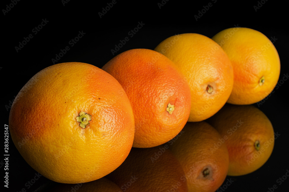 Group of four whole fresh pink grapefruit placed diagonally in line isolated on black glass