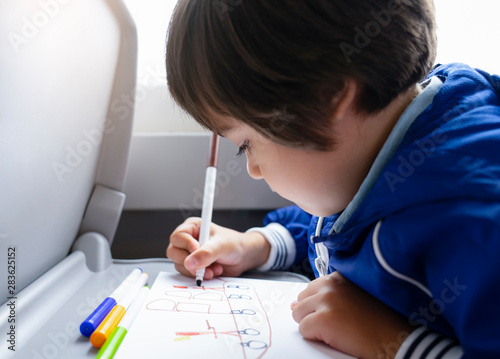 Selective focus of little boy draws with colored pen on white paper, Kid traveling by the train, Little boy in a high speed express train on family vacation, Entertainment for young passenger.