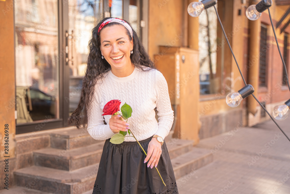 Fototapeta premium Young beautiful pretty girl with long hair with red rose in the city