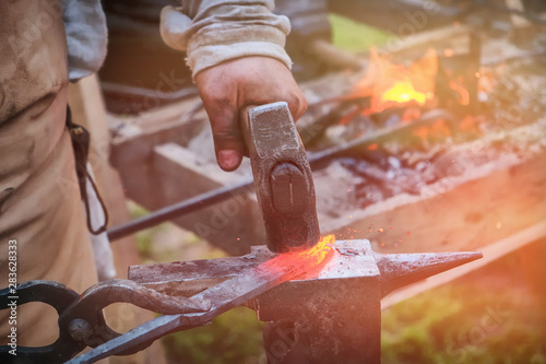 The blacksmith strikes the red blade of the sword with a hammer. Work in the forge to create weapons. The knife is between a rock and a hard place. photo