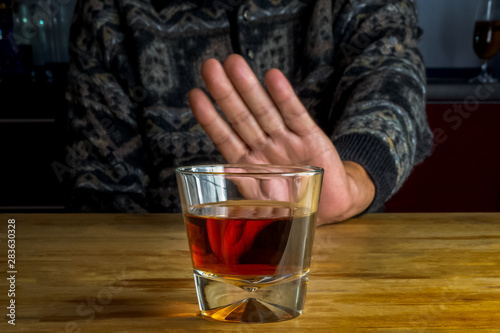 Male hand rejecting glass with alcoholic beverage on blurred background. Concept