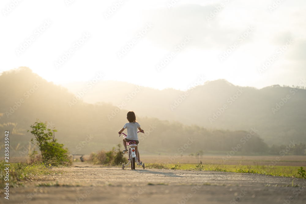 independent asian child ride her bicycle in countryside road by her self with beautiful scenery and sunset