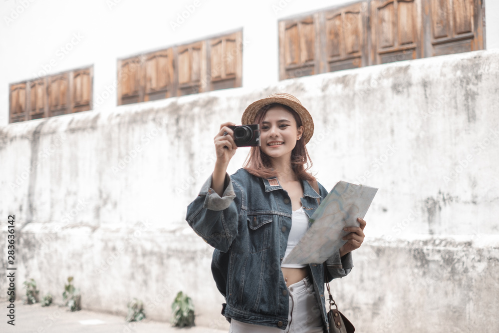 Smiling woman traveler in thapae gate landmark chiangmai thailand with backpack holding world map and camera on holiday, relaxation concept, travel concept