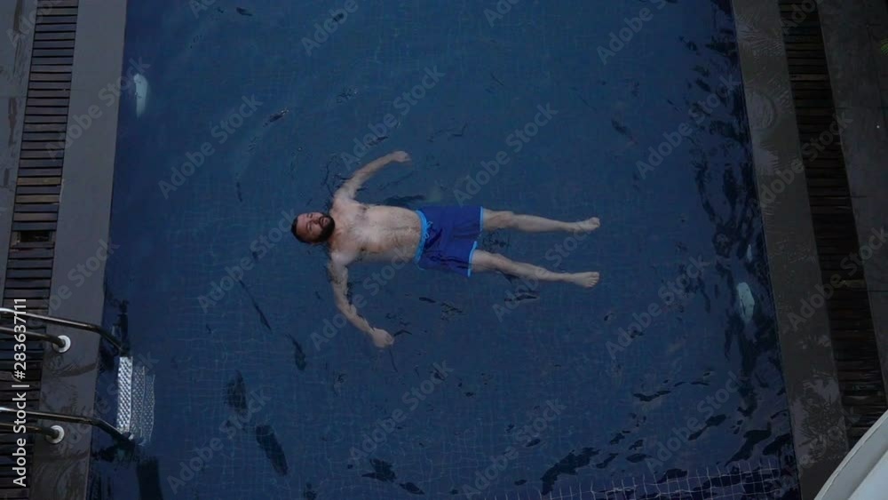 Young man floating on water in swimming pool, super slow motion Young man floating on water in swimming pool, super slow motion