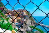 The famous village of Manarola behind the iron fence on the hill. A beautiful blue sky and sunny day of the European summer in Liguria, Italy.