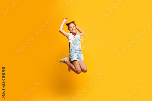 Beautiful teen girl posing with headphones over yellow background