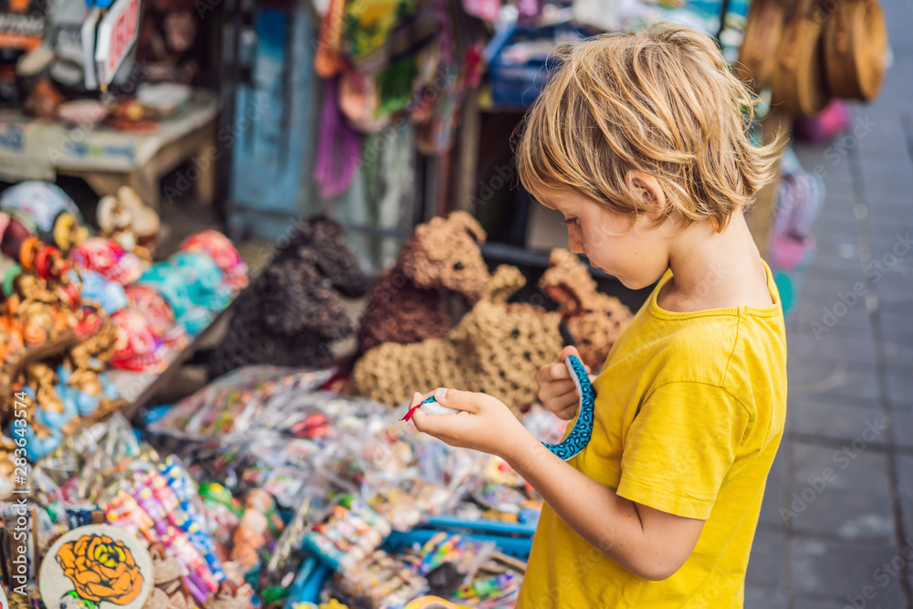 Boy at a market in Ubud, Bali. Typical souvenir shop selling souvenirs and handicrafts of Bali at the famous Ubud Market, Indonesia. Balinese market. Souvenirs of wood and crafts of local residents Boy at a market in Ubud, Bali. Typical souvenir shop selling souvenirs and handicrafts of Bali at the famous Ubud Market, Indonesia. Balinese market. Souvenirs of wood and crafts of local residents