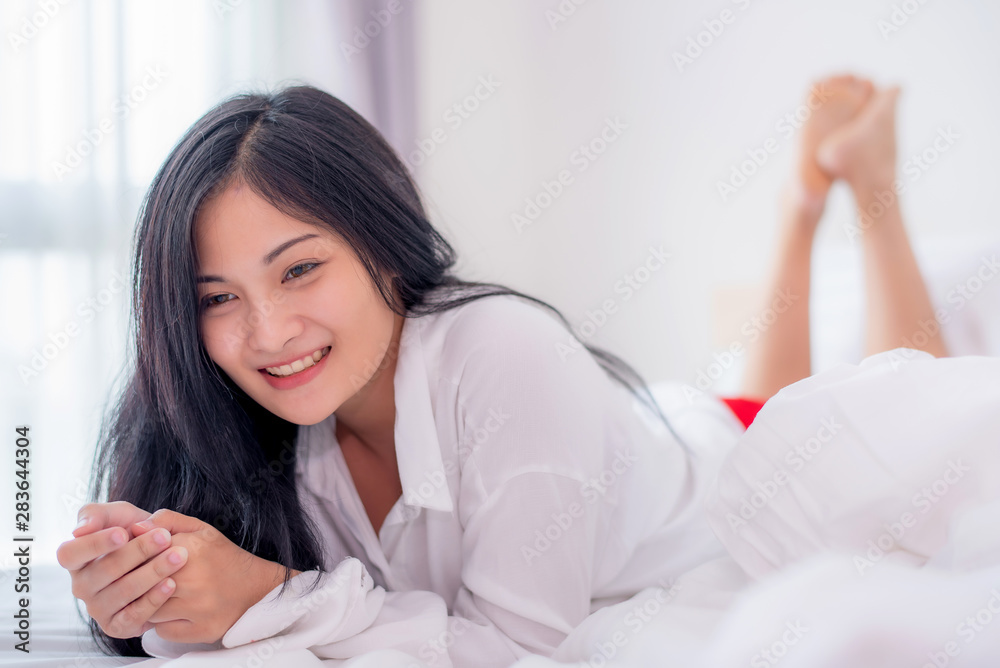 Beautiful young pretty Asian woman wake up and make happy smile with white shirt at the white bed in the morning. Beautiful young pretty Asian woman wake up and make happy smile with white shirt at the white bed in the morning.