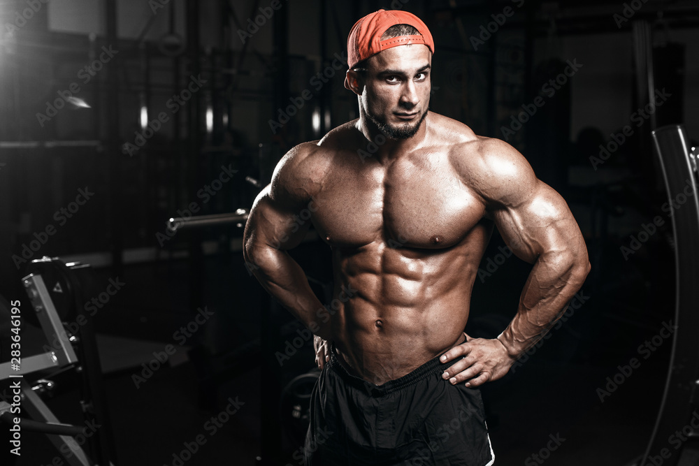 Muscular athletic bodybuilder fitness model posing after exercises in gym