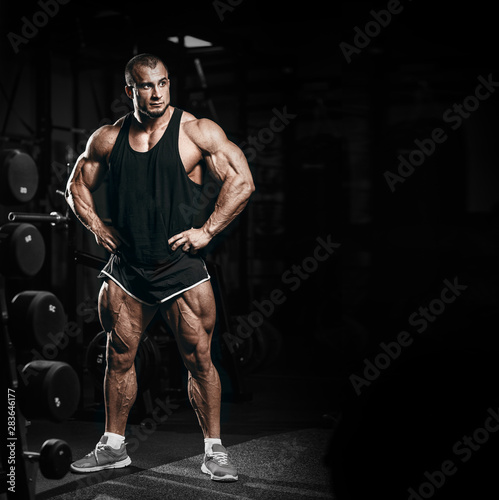 Muscular athletic bodybuilder man in gym over dark background with dramatic light posing and resting after hard training work out. Sport bodybuilding photo concept with copy space