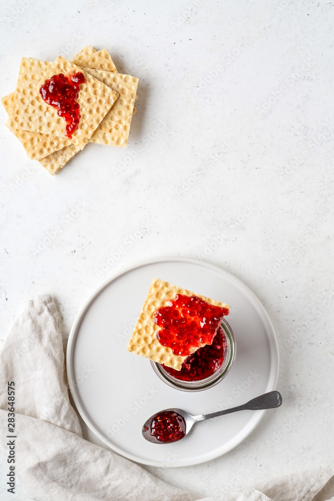 Toast crispbreads with raspberry jam served on round plate. Raspberry jam in a glass jar. Toast crispbreads with raspberry jam served on round plate. Raspberry jam in a glass jar.