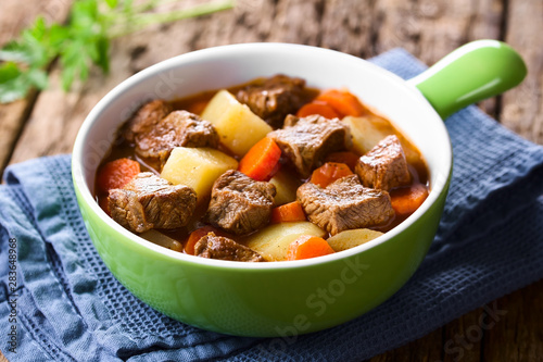 Fresh homemade beef stew with carrot and potatoes served in green bowl (Selective Focus, Focus one third into the stew)