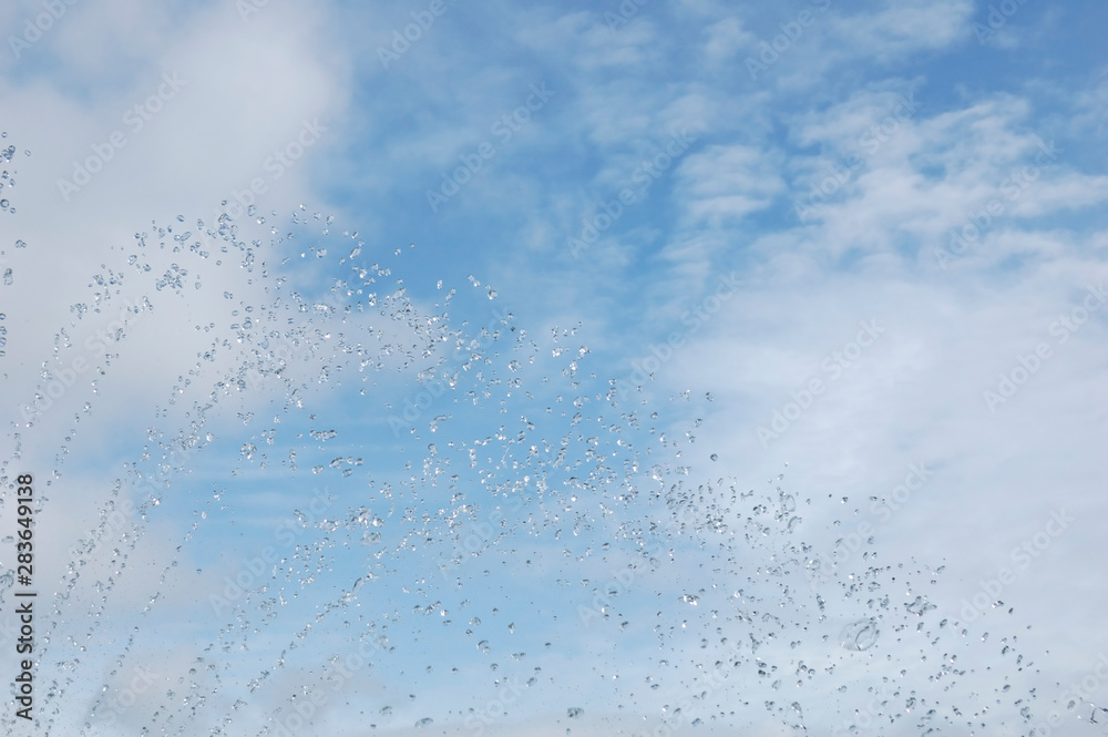 Splashes and drops of water, pleasantly formed by a fountain. on the background, the blue sky with white clouds. Splashes and drops of water, pleasantly formed by a fountain. on the background, the blue sky with white clouds.