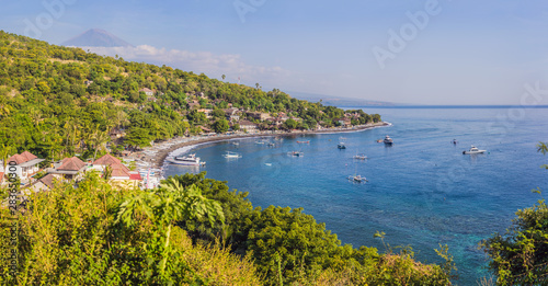 Aerial view of Amed beach in Bali, Indonesia. Traditional fishing boats called jukung on the black sand beach and Mount Agung volcano in the background, partially covered by clouds