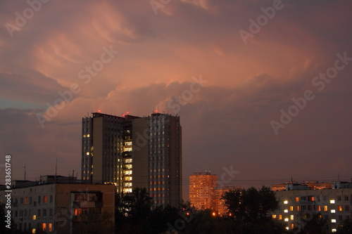 Top view on multi-storey houses under a pink sky with cirrus clouds over the night city