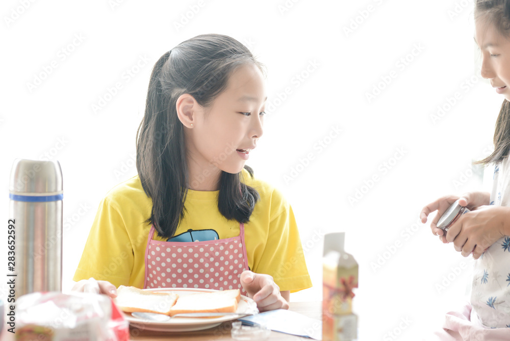 Asian sister spreading strawberry jam on bread for her younger sister, lifestyle concept. Asian sister spreading strawberry jam on bread for her younger sister, lifestyle concept.