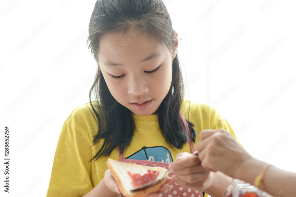 Asian sister spreading strawberry jam on bread for her younger sister, lifestyle concept. Asian sister spreading strawberry jam on bread for her younger sister, lifestyle concept.