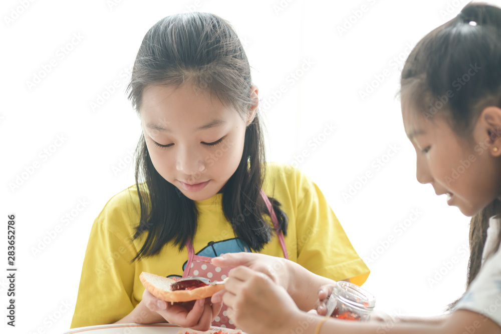 Asian sister spreading strawberry jam on bread for her younger sister, lifestyle concept. Asian sister spreading strawberry jam on bread for her younger sister, lifestyle concept.