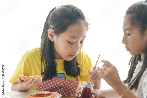 Asian sister spreading strawberry jam on bread for her younger sister, lifestyle concept. photo