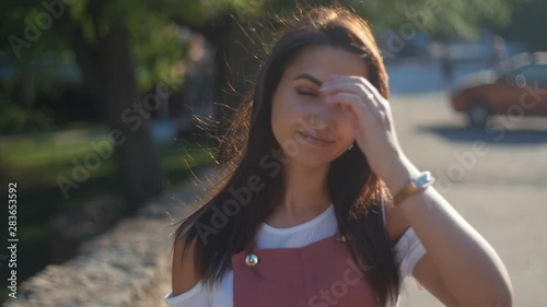 Young brunette cute girl playing with hair on the street near the park at sunset