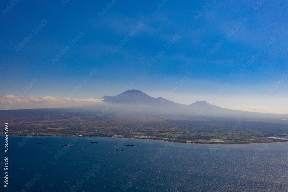 Aerial drone view of beautiful seascape with boats over island with volcano background in Indonesia