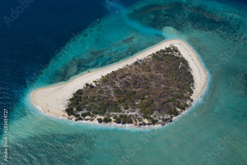 Aerial drone view of small exotic island surrounded by coral reef and blue sea