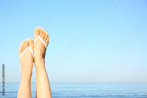 Closeup of woman wearing flip flops near sea, space for text. Beach accessories