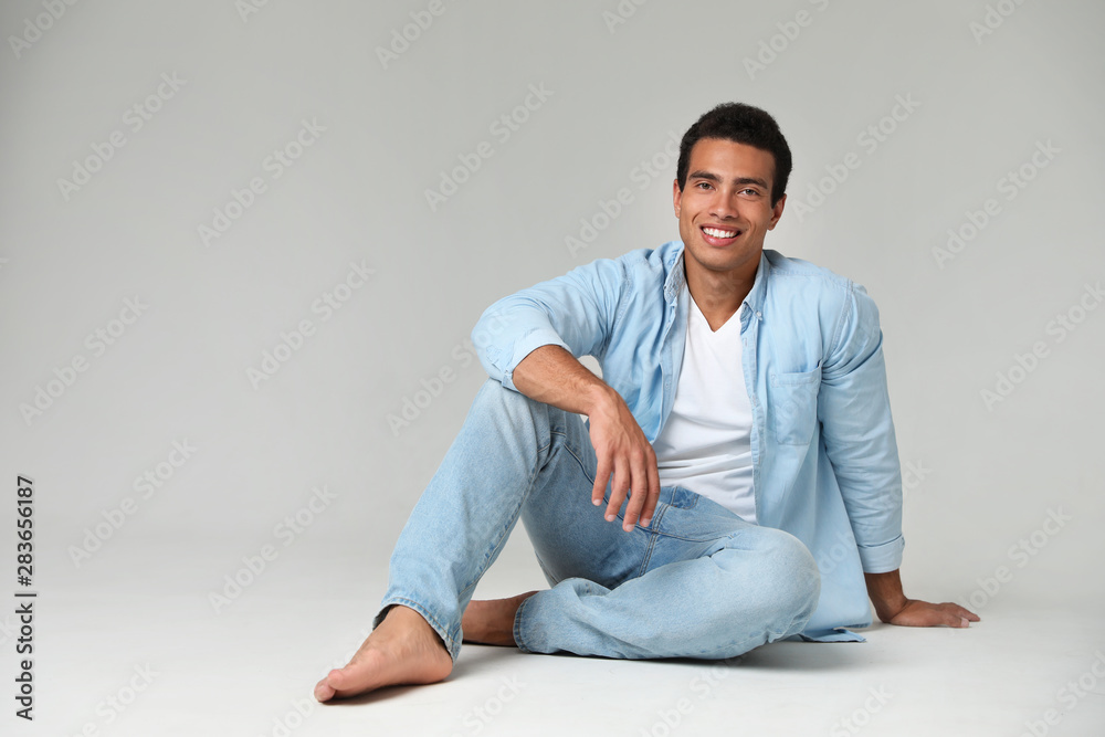 Handsome young African-American man sitting on light background. Space for text Handsome young African-American man sitting on light background. Space for text