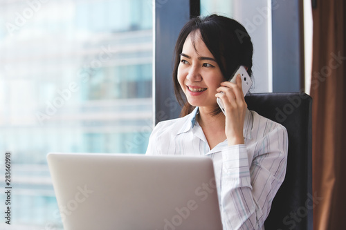 Asian business woman in smile face are using mobile phones and laptops in the office.