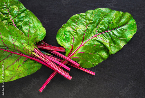 Rhubarb on black background. Fresh red rhubarb stalks with green leaves, top view.