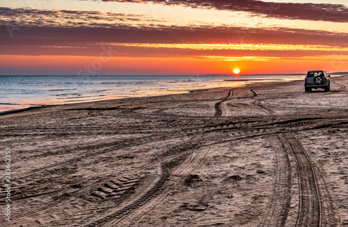Fototapeta Naklejka Na Ścianę i Meble -  Sunrise on sandy beach of the Baltic Sea with tracks of cars