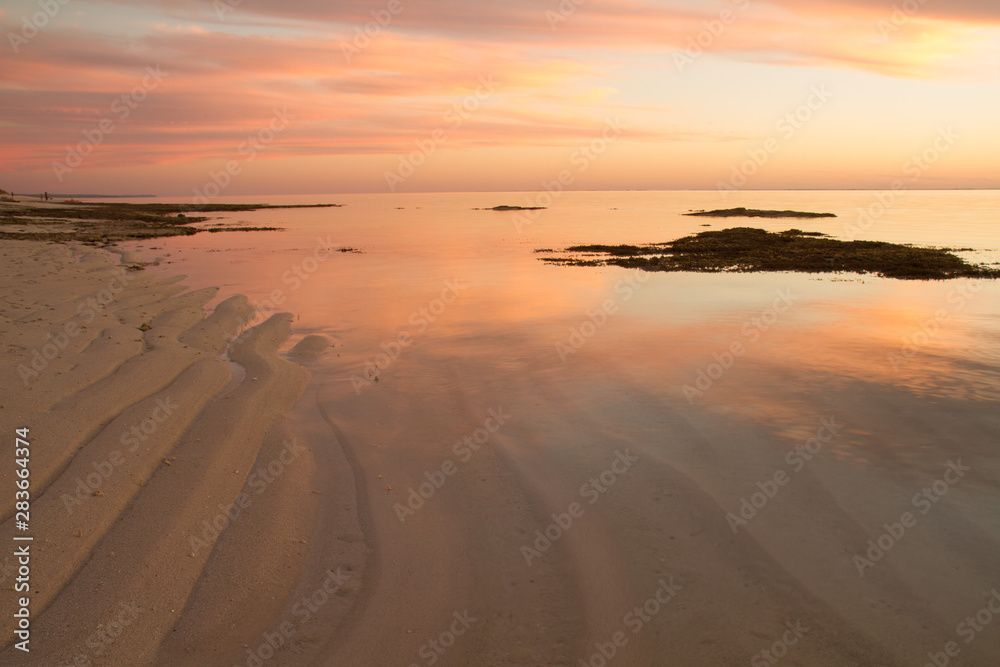 Colored evening sky reflected in shallow sea over rippled sand base.