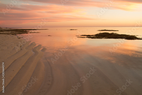 Colored evening sky reflected in shallow sea over rippled sand base.