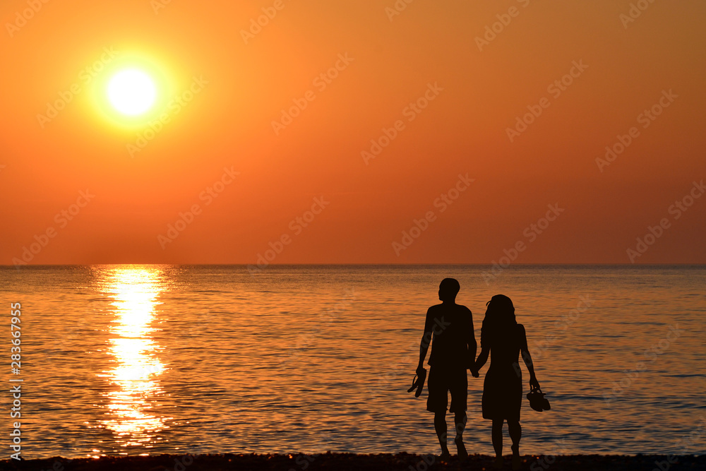 Back view of a couple silhouette walking together on the beach at sunrise in summer