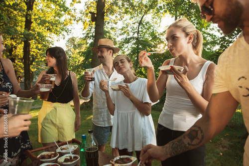 Canvas Print Group of happy friends eating and drinking beers at barbecue dinner on sunset time