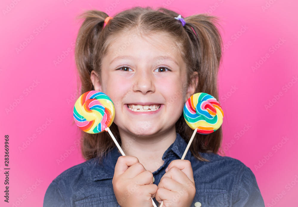 Happy smiling child with sweet lollipop having fun over colorful pink background