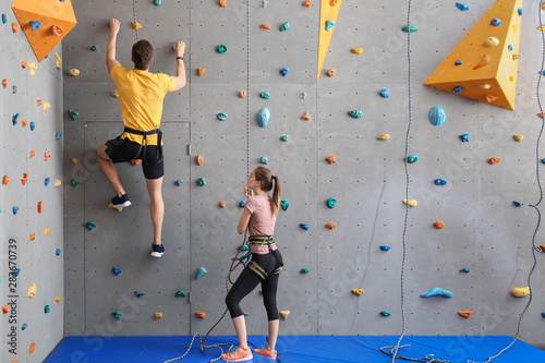 Young man with instructor climbing wall in gym