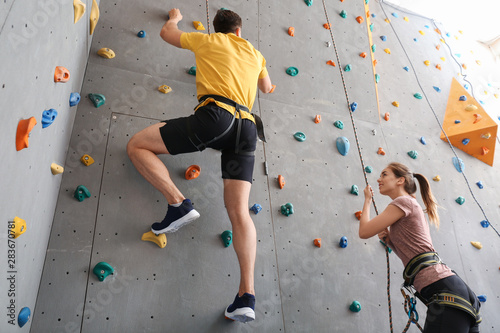 Young man with instructor climbing wall in gym