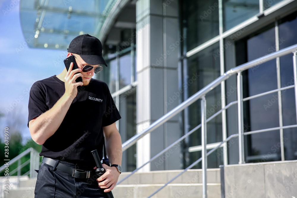 Handsome male security guard talking by phone outdoors Handsome male security guard talking by phone outdoors