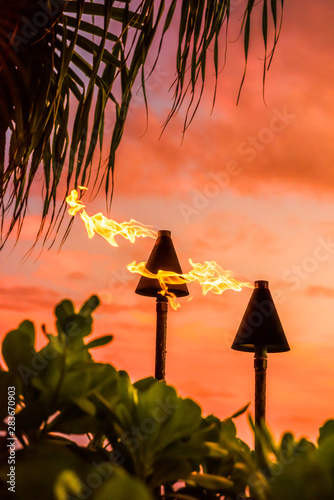 Hawaii luau party Maui fire tiki torches with flames burning against sunset sky clouds at night. Hawaiian culture travel background.